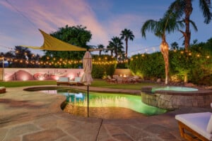 Private pool, hot tub and fire pit lit at dusk in the palm-lined backyard of Coachella Sol Haus, a family vacation rental in Indio, California